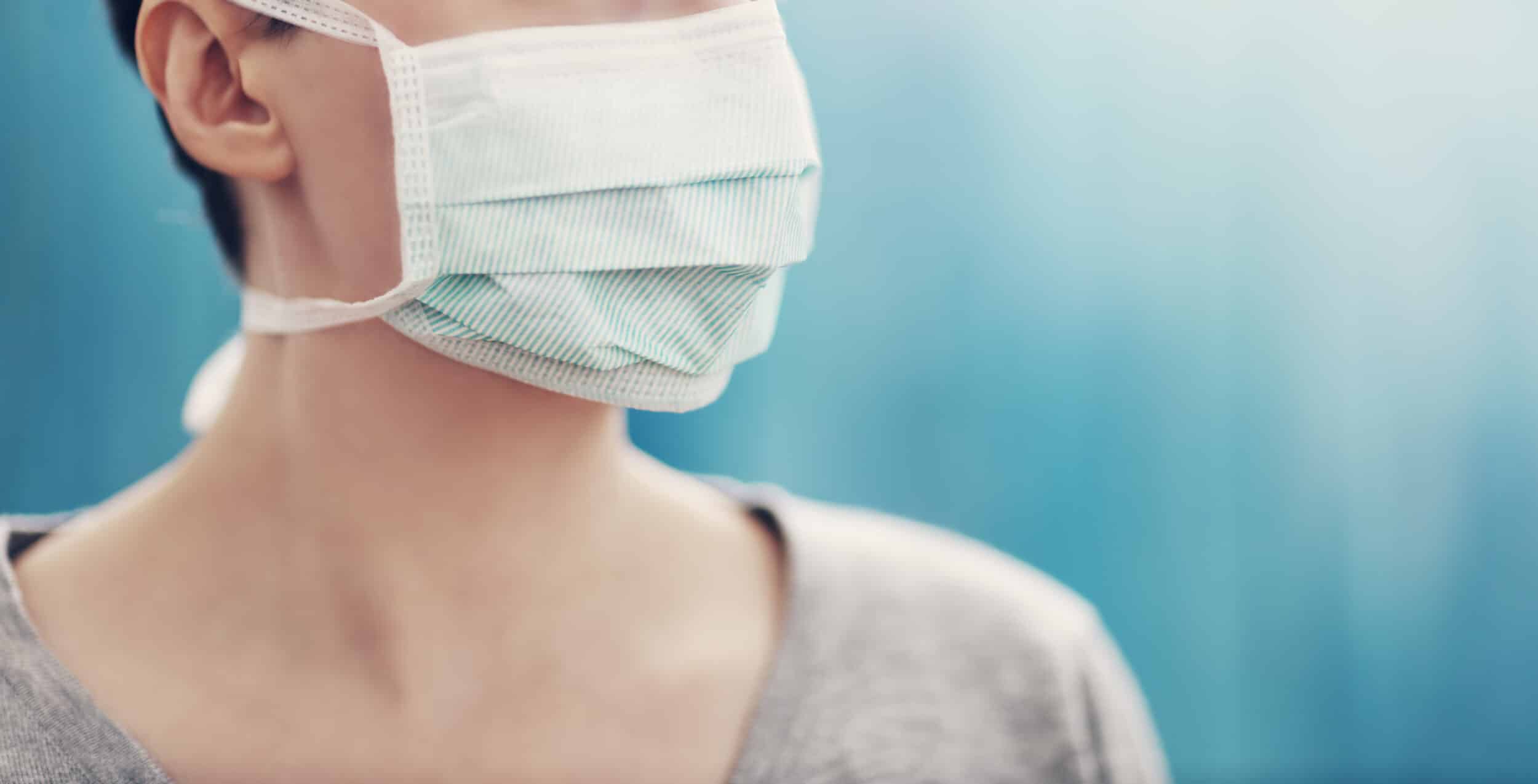 young woman in medical face protection mask indoors on blue background
